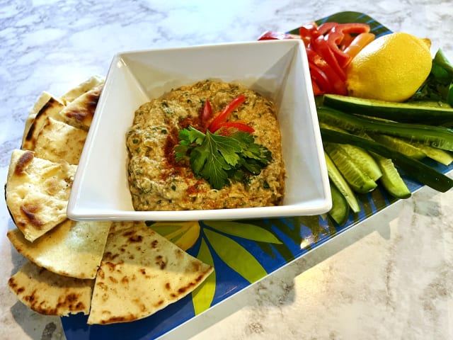 baba ganoush on a blue platter alongside pita triangles, cut cucumber, red bell peppers and a lemon