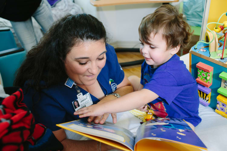 photo of a pediatric clinic setting where a female provider is reading a book with a young child