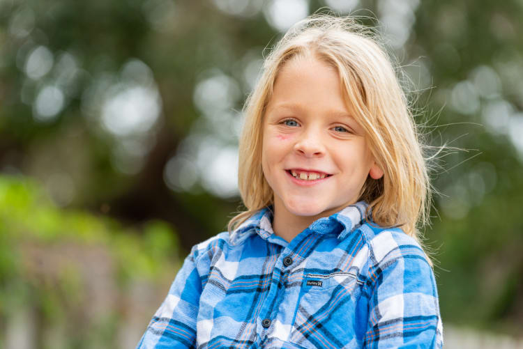 smiling young boy with blonde hair outside in a flannel shirt
