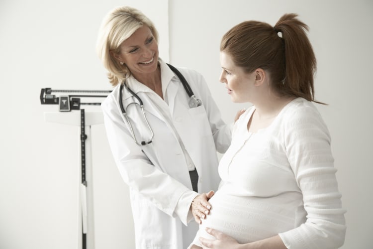 Female doctor touching pregnant woman's stomach, smiling