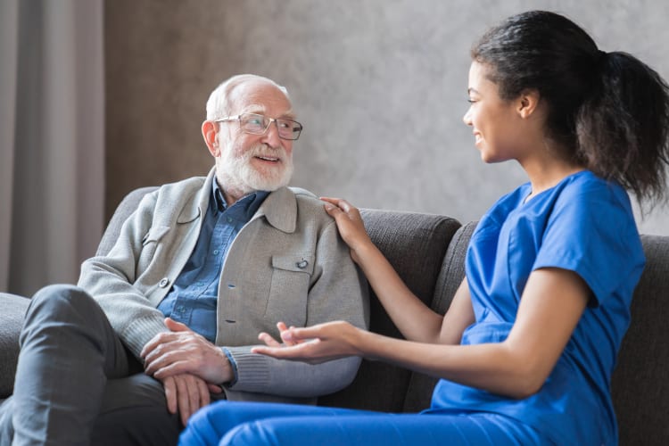 A caring black nurse talks to an elderly senior male patient sitting in the living room at a homecare visit