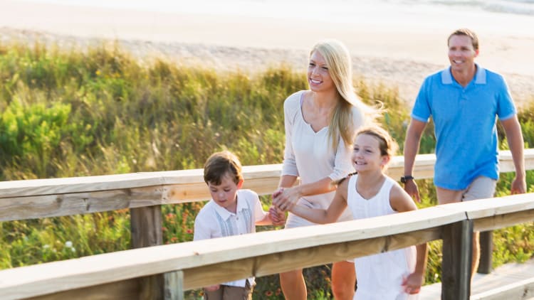 smiling family holding hands walking on a boardwalk at the beach