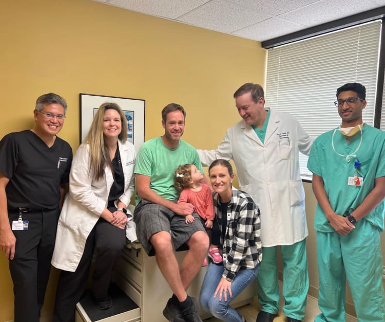 Caroline Holstein and her parents pose with Dr. Hanel, Dr. Aldana and other care team members at a follow-up appt