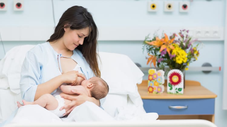 nursing mom with newborn baby and fresh bouquet of flowers by her bed in hospital birthing center