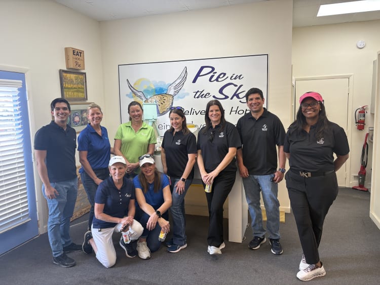 a team of smiling Baptist Health team members in front of a pie in the sky sign before they start their volunteer shift.