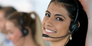 woman with dark long hair wearing a telephone operator headset smiling at you