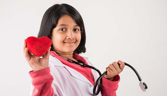 young girl wearing a lab coat and stethoscope and holding a plush heart toy