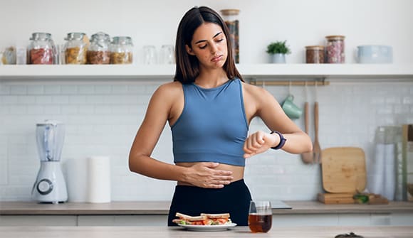 A woman looking at her watch and hold her stomach like she's hungry