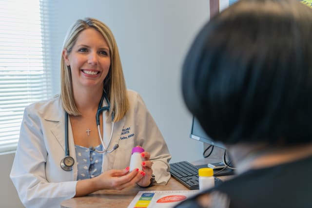 a smiling female provider wearing a stethoscope sits across a desk from a patient