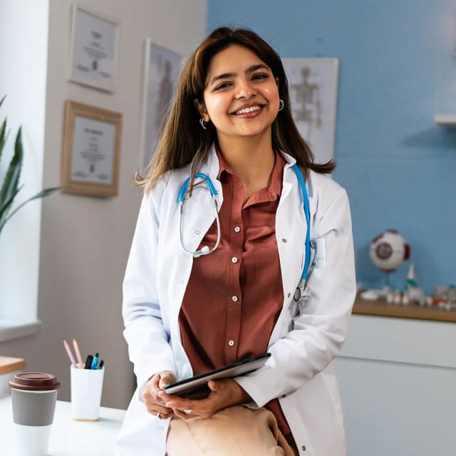 a female doctor smiling in a white coat with stethoscope around her neck.