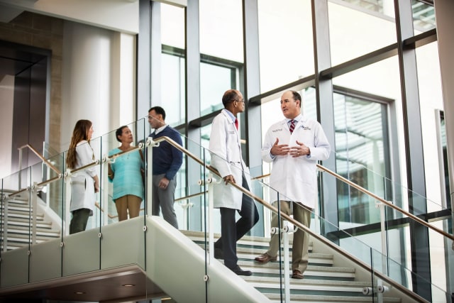 groups of doctors and patients having conversations while walking down the stairs in a brightly lit lobby.