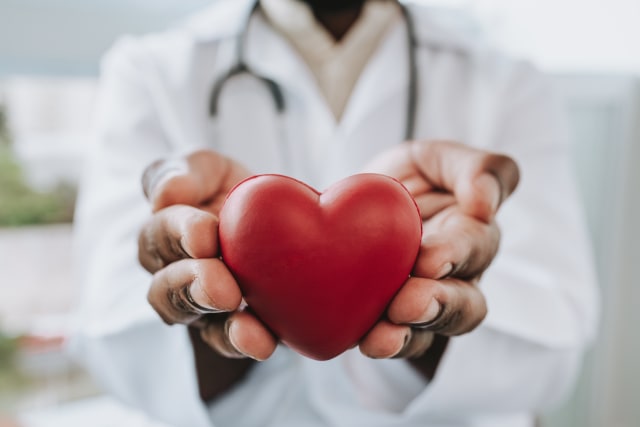 man in a doctor coat holding a red heart-shaped squeeze toy