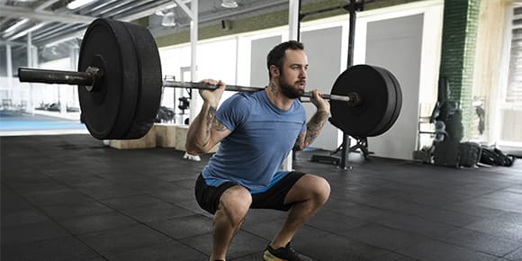 man squatting weights in a gym