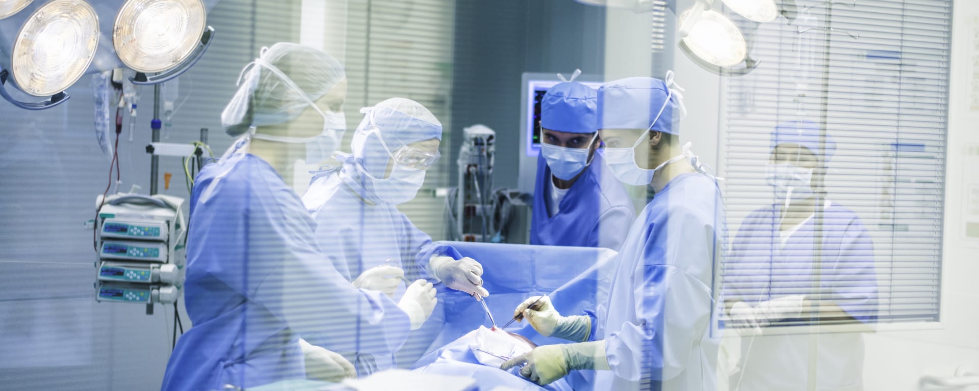 Surgeon team operating, shot through glass wall.