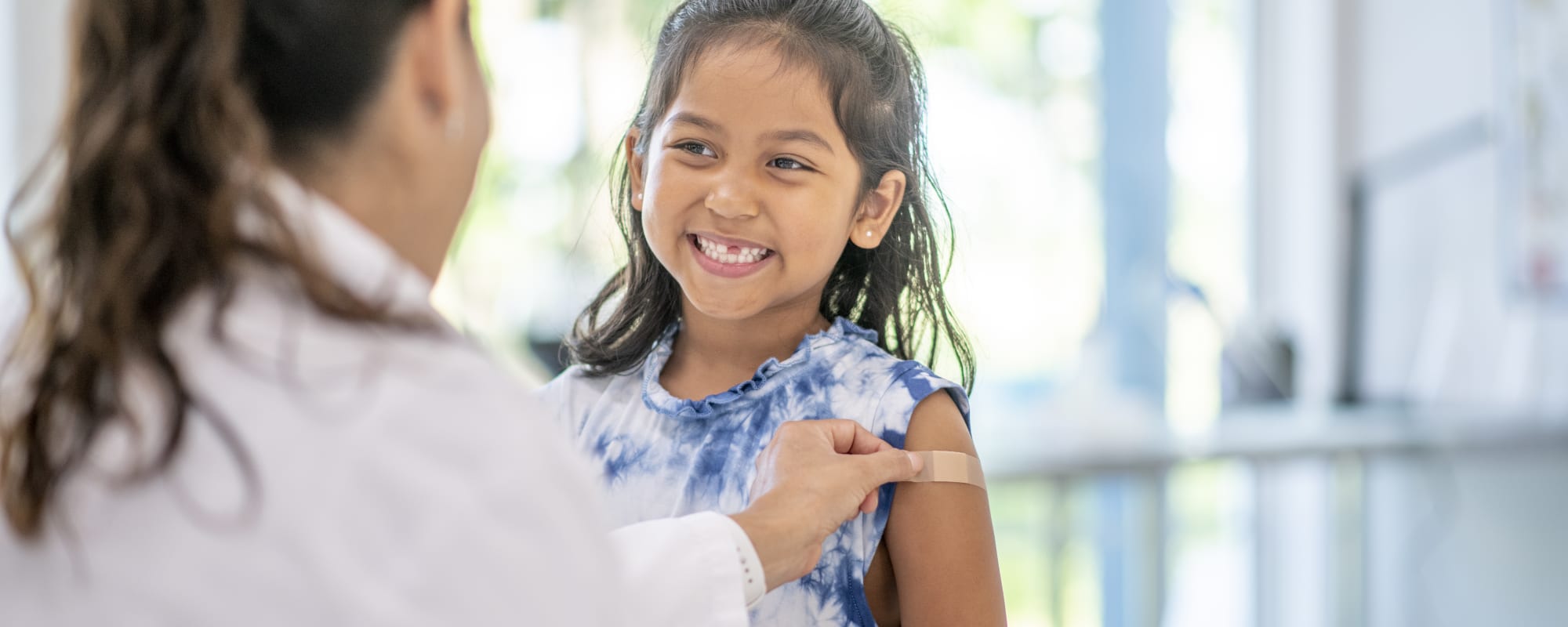 child interacts with the female Hispanic doctor at a medical appointment.