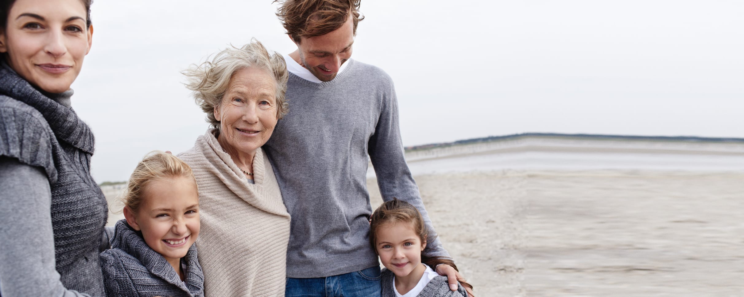 A grandmother at the beach with her children and grandchildren, all smiling at the camera.
