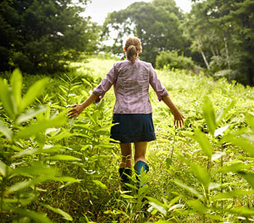 woman walking in a field touching plants