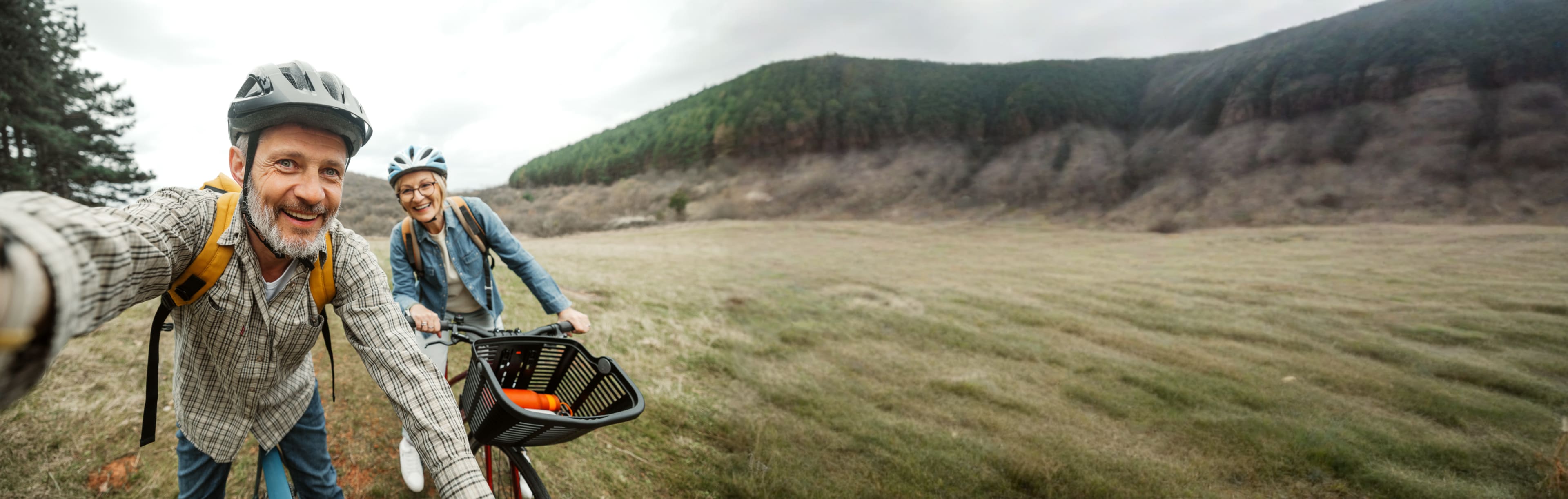 An older man and woman biking through a hilly area