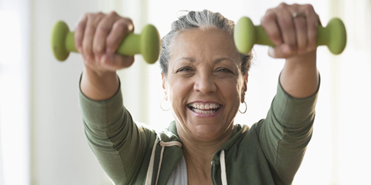 older Hispanic woman lifting weights in living room