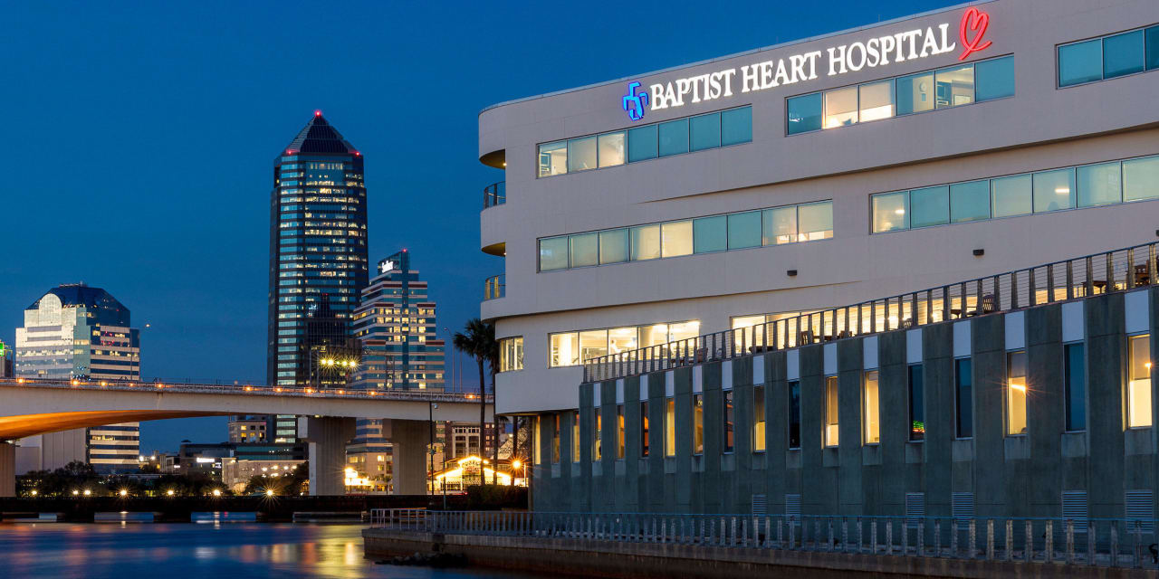 A nighttime photograph of the Baptist Heart Hospital exterior from the St. Johns River with city buildings in the background.
