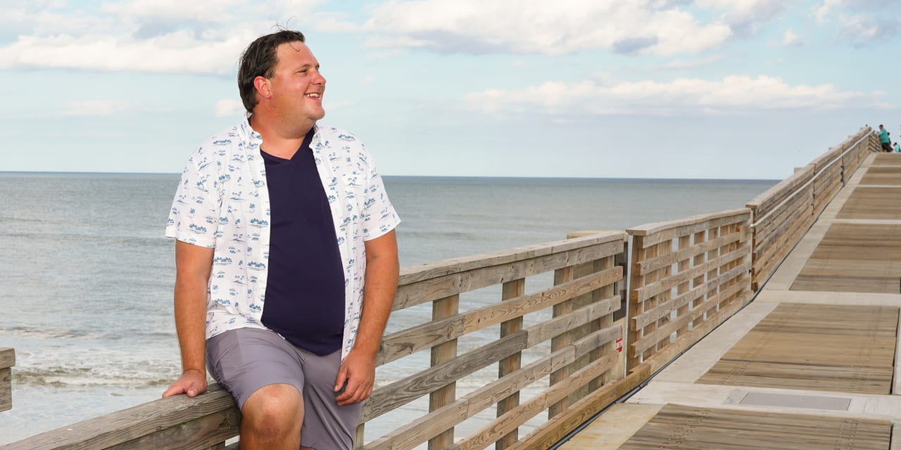 slightly smiling man leaning on a boardwalk at the beach