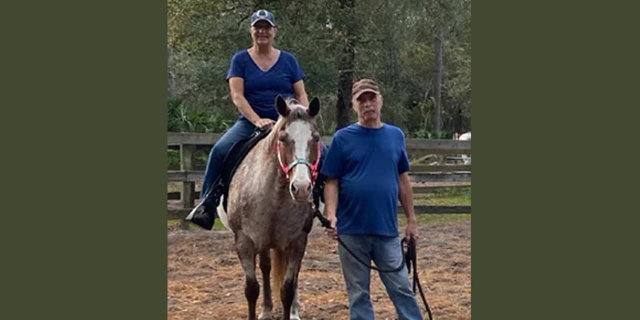 A women on a horse with a man standing beside the horse and the woman.