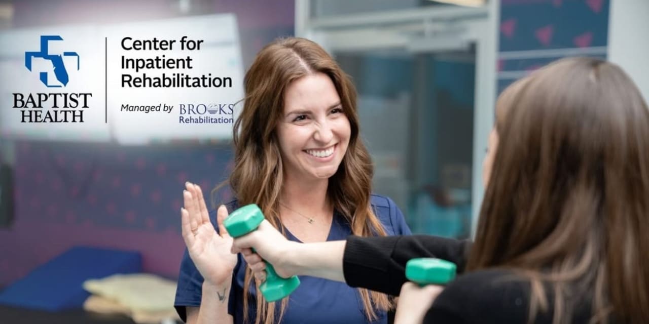 woman uses dumbbells while a therapist looks on