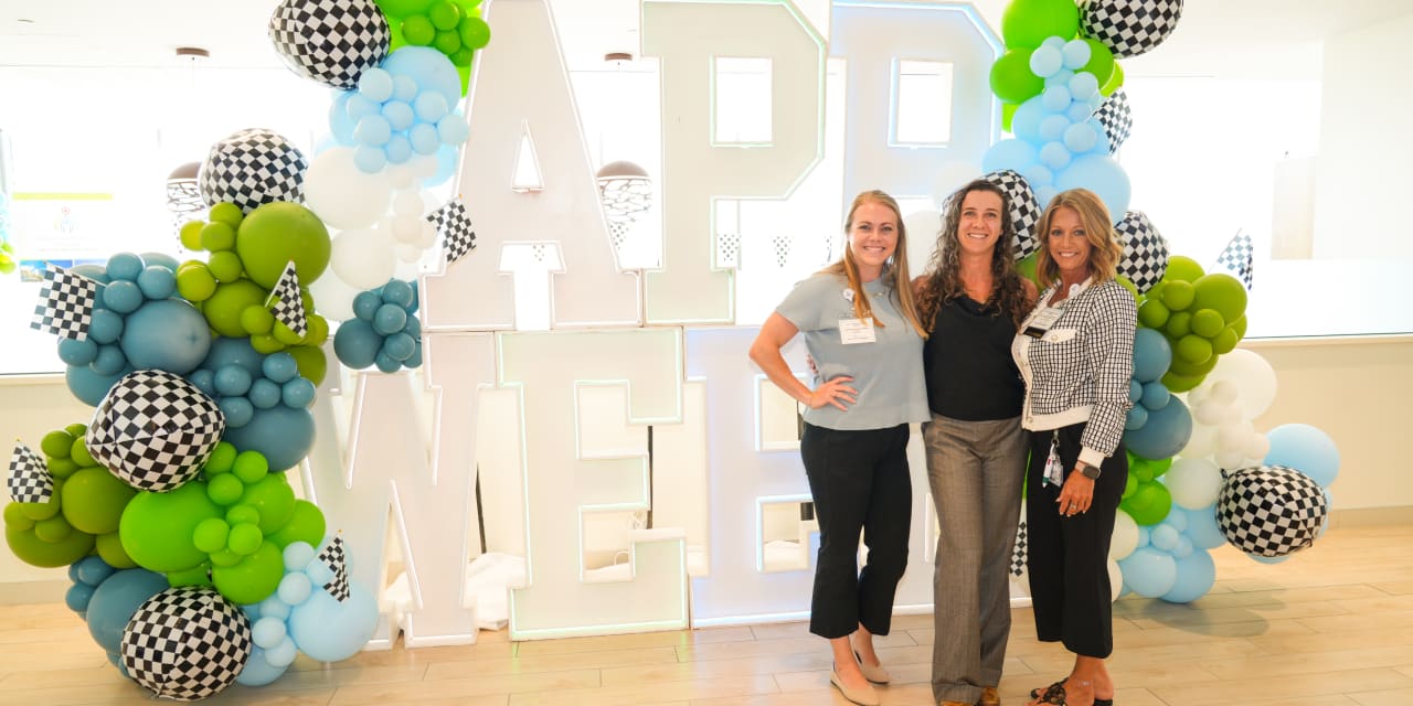 Three female advanced practice providers standing in front of a large sign that says "APP Week"