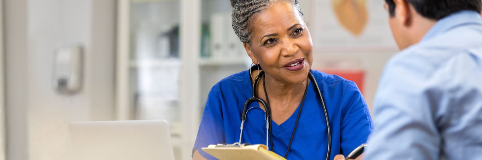 physician with a clipboard talking to a man in a medical office
