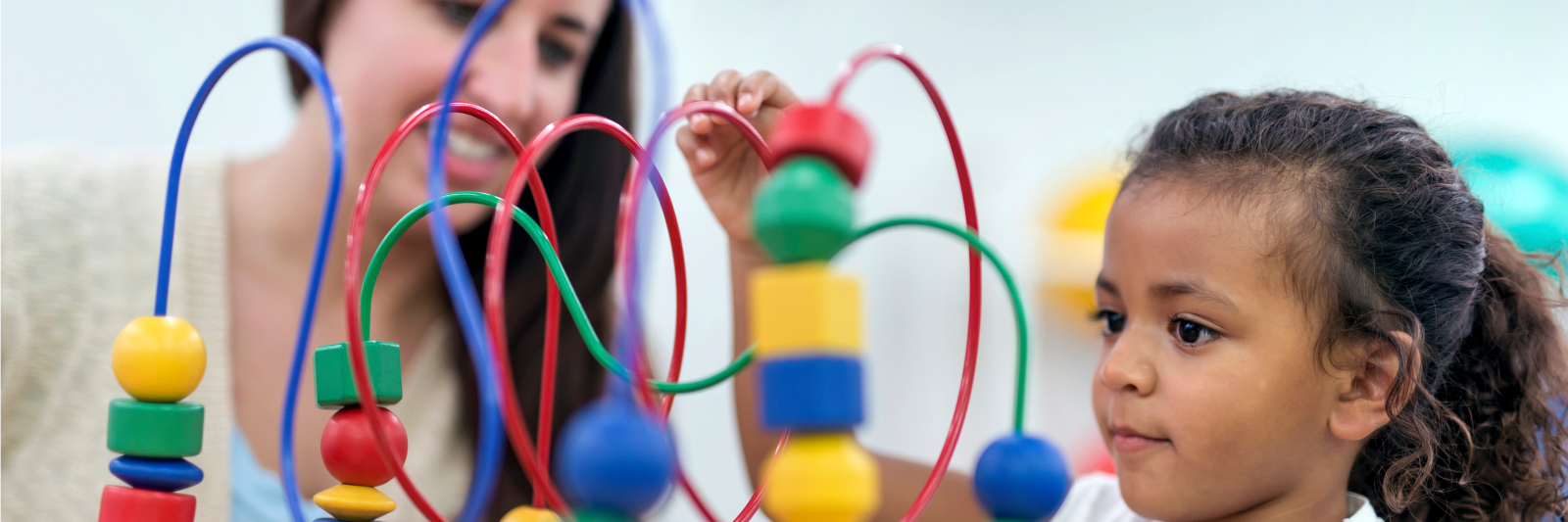 photo of a young girl playing with a colorful block toy as a woman looks on