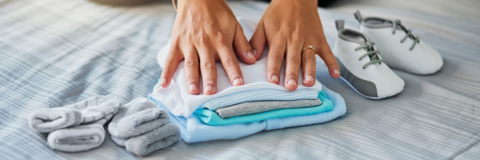 close up of a woman's hands folding baby clothes, socks and shoes