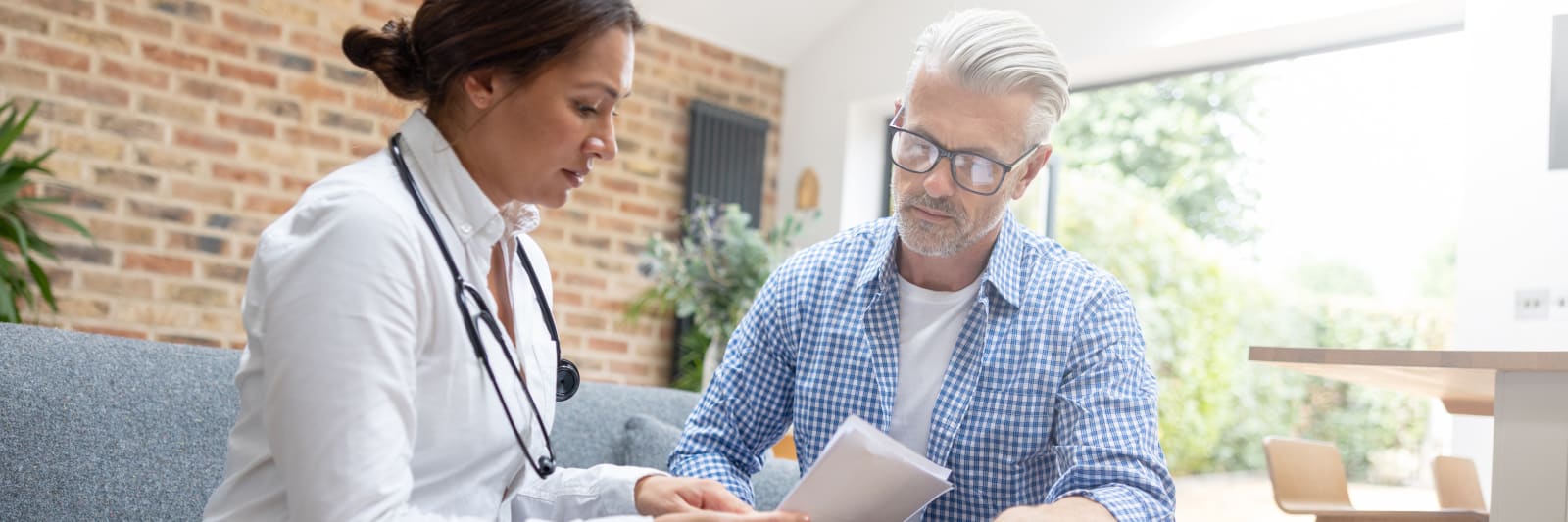 A female doctor and a middle-aged male patient looking at paperwork together  while discussing treatment for his hemorrhoids.