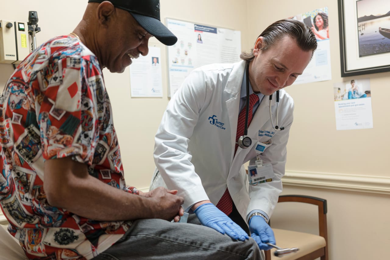 smiling male doctor testing the reflexes of a smiling male patient