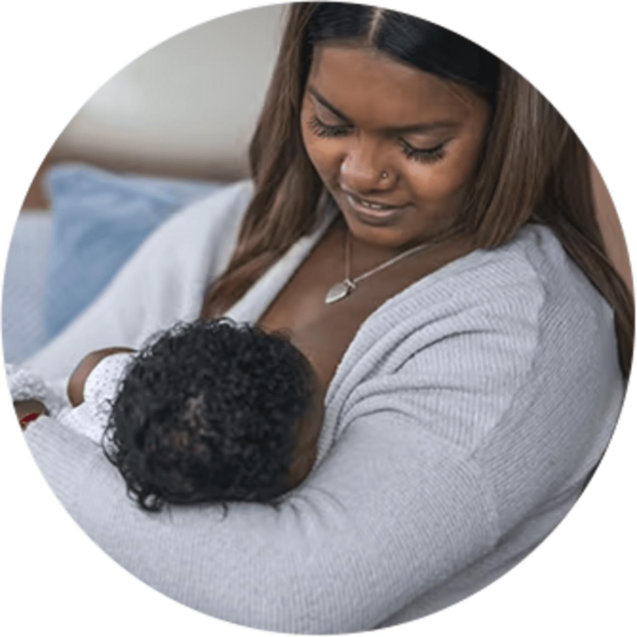 A smiling woman breastfeeding her baby daughter on a couch in her home.