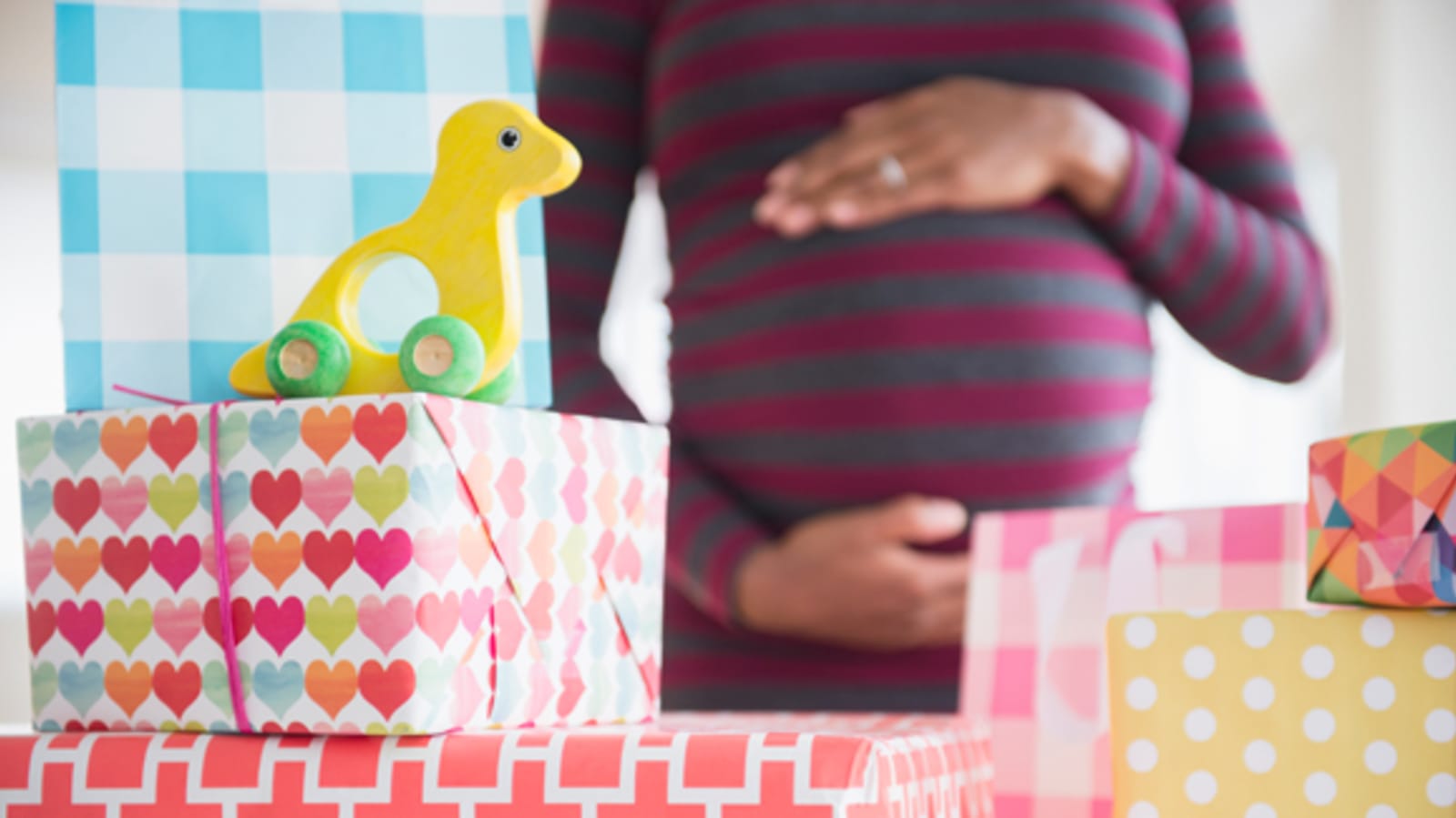 Woman holds baby bump, stack of gifts in foreground.