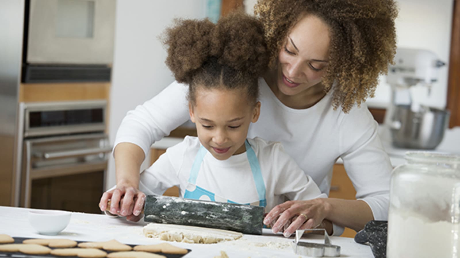 A mother and daughter roll out cookie dough together while baking.