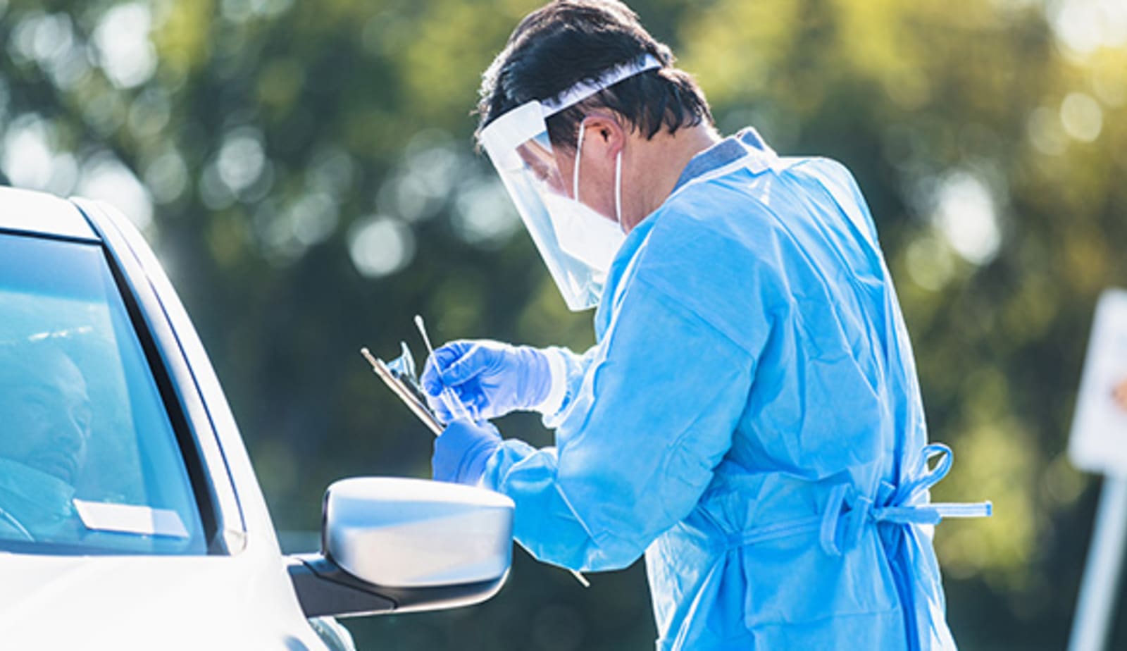fully gowned man preparing a COVID-19 swab test to give someone inside their car