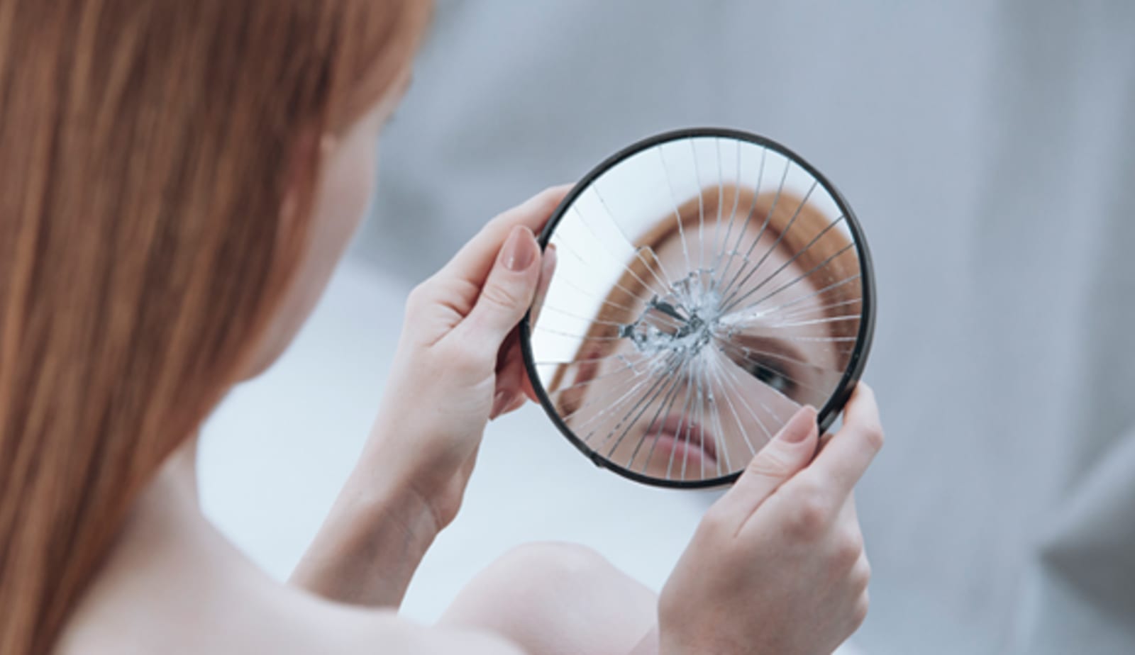 A woman looking at a broken mirror