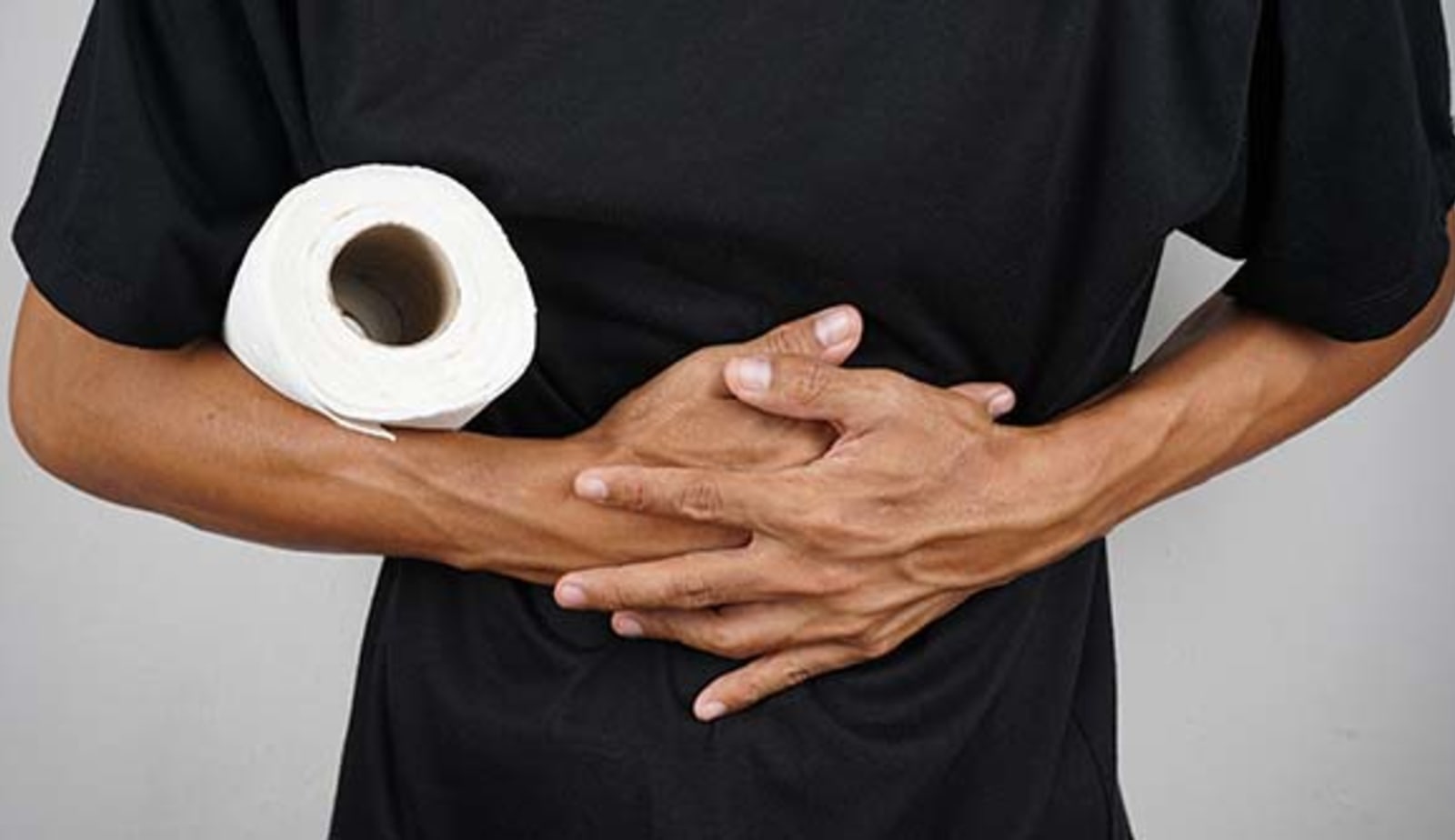 man holding toilet paper and gripping his stomach with both hands