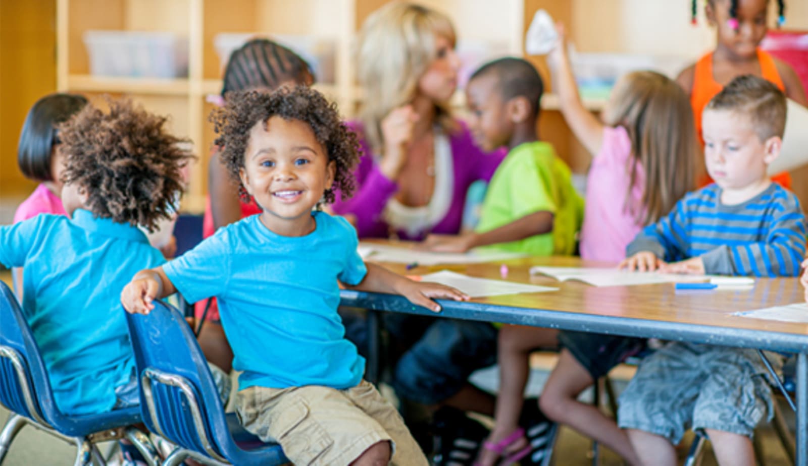 young preschool age child smiles at the camera while sitting at a table with classmates