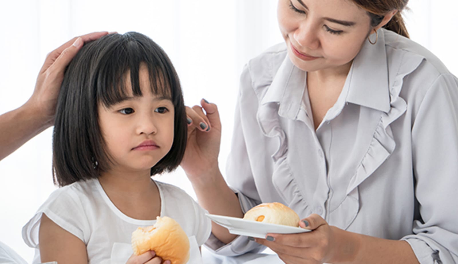 Woman sitting next to her child helping her eat food. 