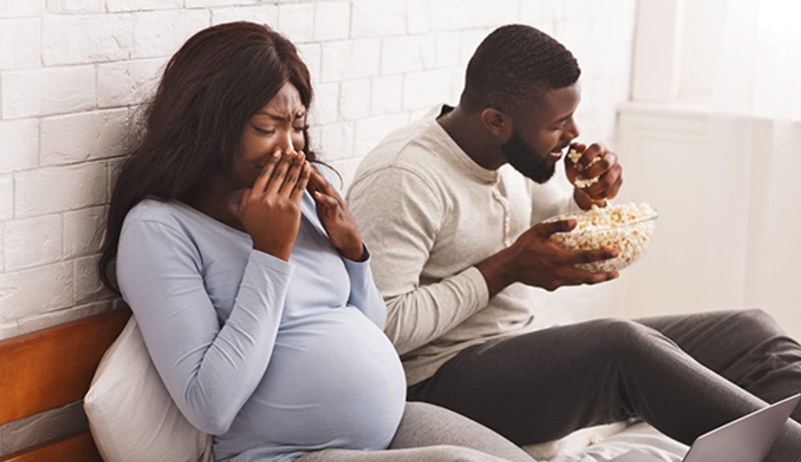 pregnant women with hands to her nose experiencing sensitivity of smell to man eating popcorn