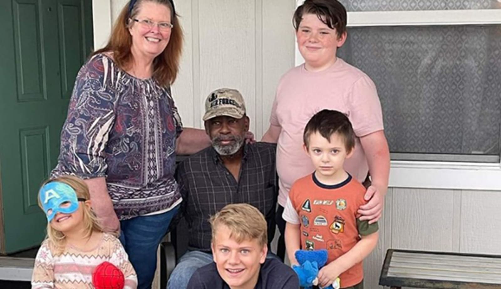 fmily stands together and smiles. two grandparents, two young boys and a young girl