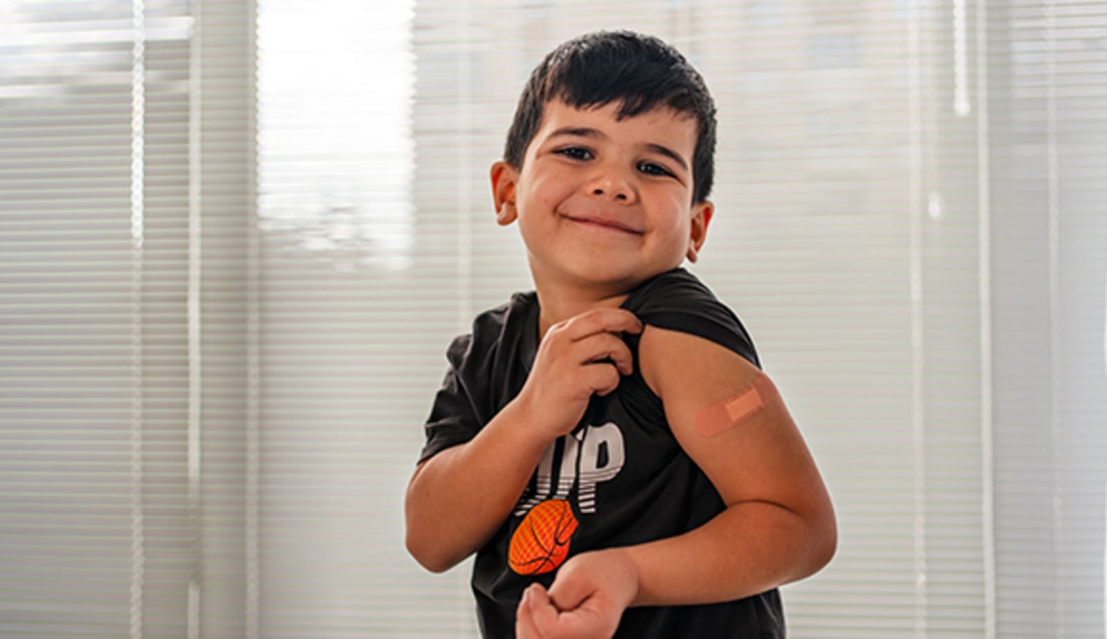 Little boy shows off bandage on upper arm regarding a shot