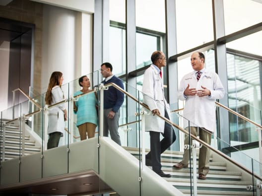groups of doctors and patients having conversations while walking down the stairs in a brightly lit lobby.