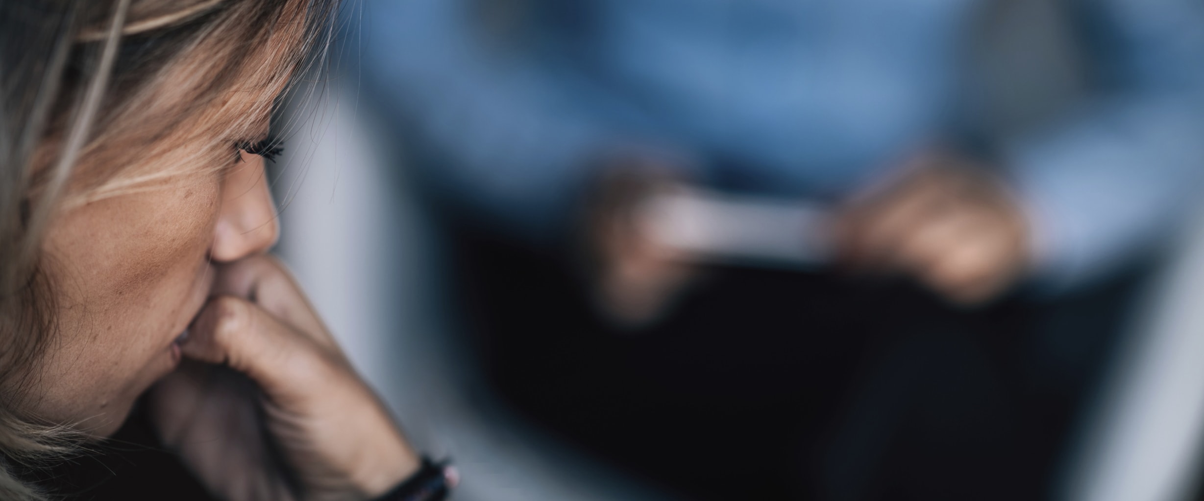 side of a woman's face as she's biting her nails while talking to a mental health counselor