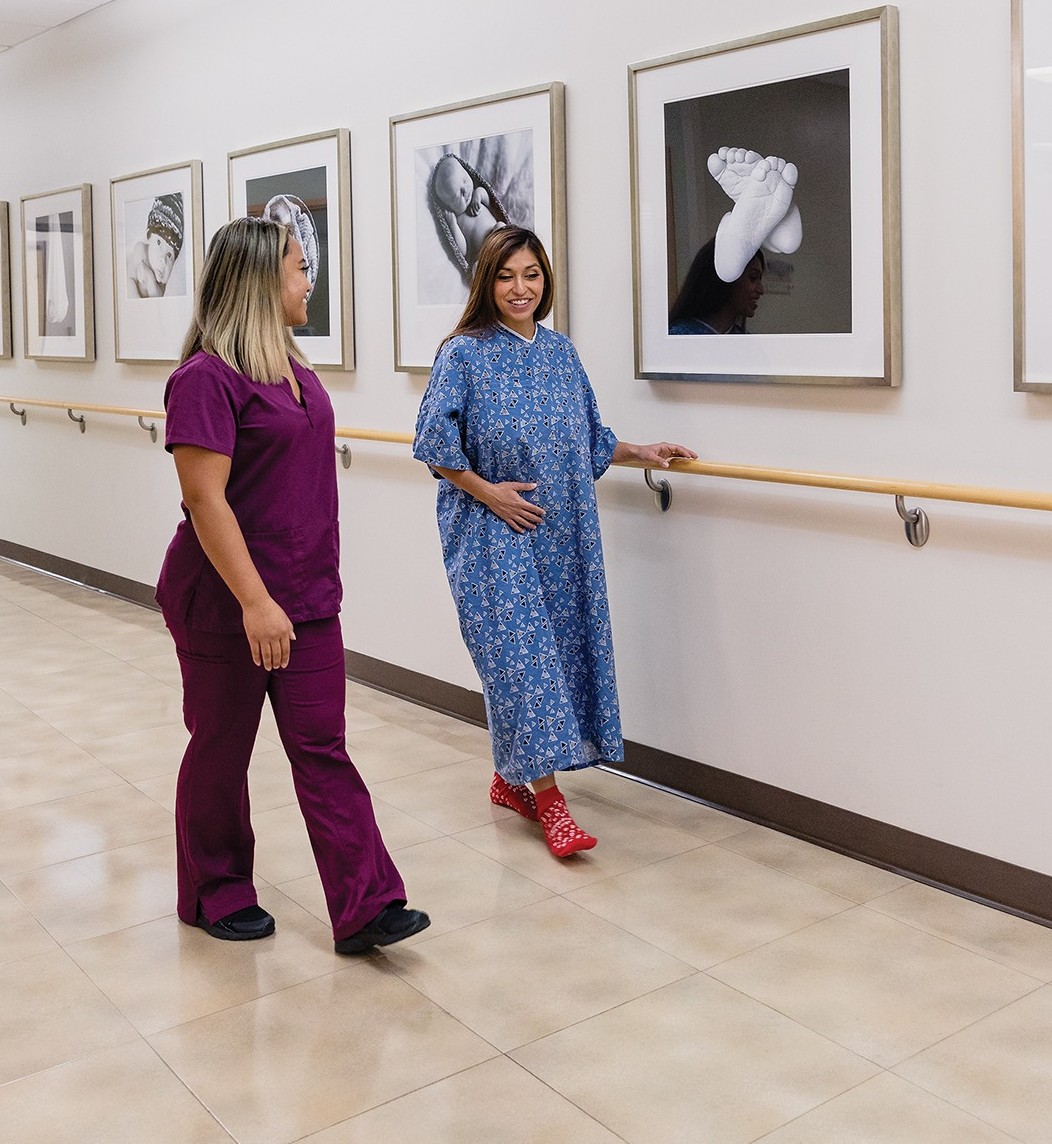 a woman in labor happily walks down the hallway with her labor and delivery nurse