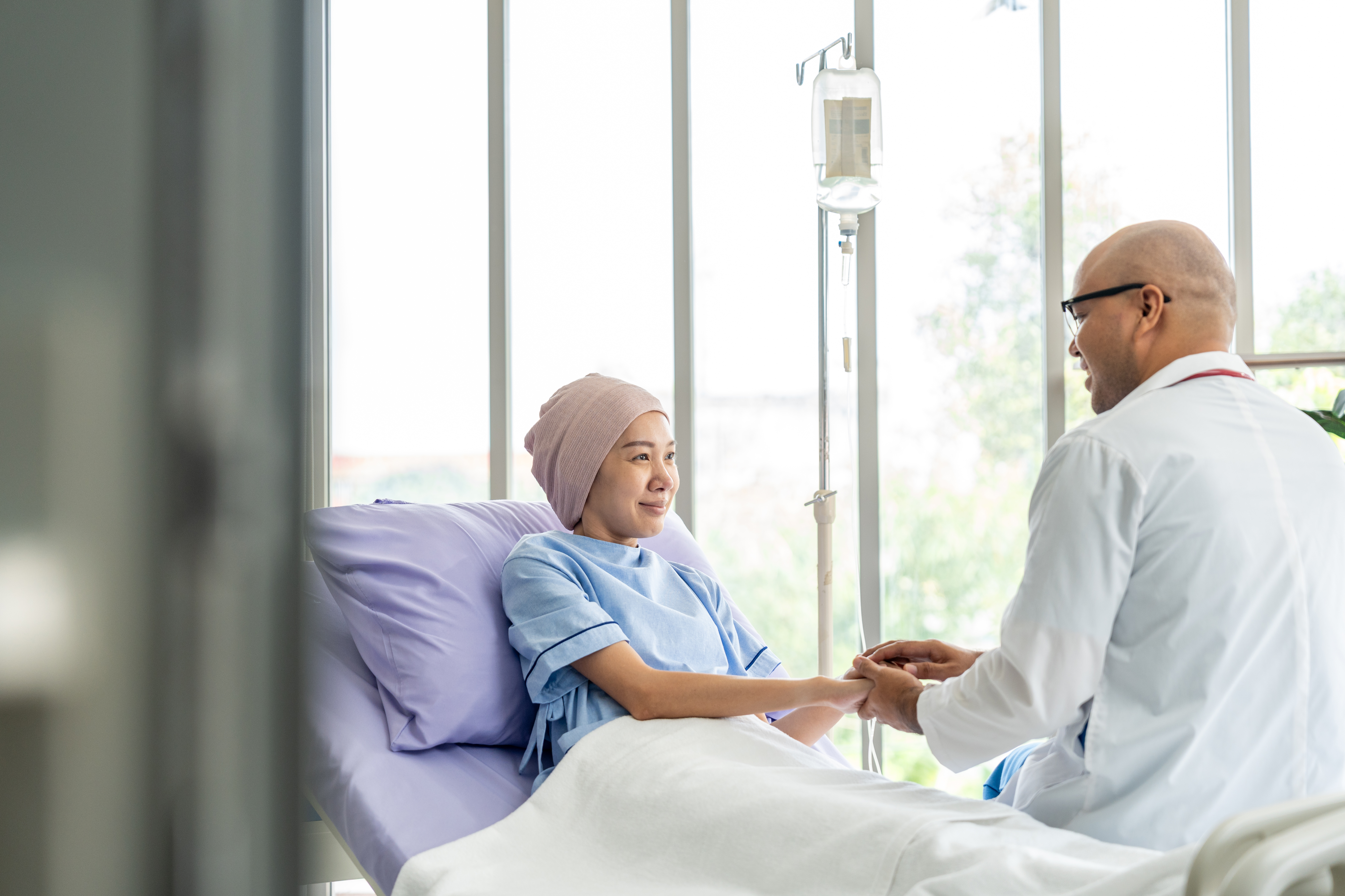 Male doctor visiting female cancer patient holding her hand in a hospital room.